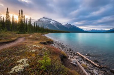 Cinematic wide landscape of Canada’s national parks with mountains, pine forest, turquoise lake, and tundra under dramatic golden-hour light.